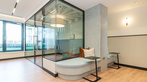 A modern room with a glass partition, a cushioned bench, a small table, and a patterned wall. - The Cornerstone One by Dublin At Home (Dublin)