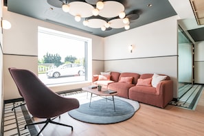 Een moderne woonkamer met een bank, een fauteuil, een salontafel en een groot raam met uitzicht op een auto.