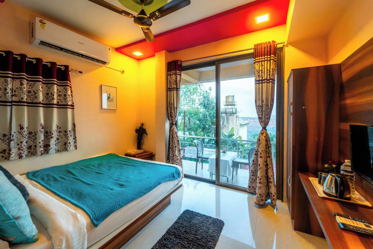 A bedroom with a bed, a TV, a desk, and a balcony with curtains.