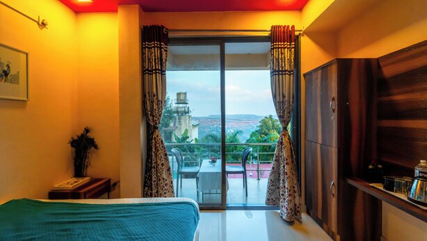 A bedroom with a bed, a nightstand, a dresser, and a balcony with a view. - Strawberry County (Mahabaleshwar)