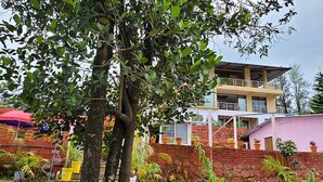 A two-story building with a balcony, surrounded by a garden with various potted plants and a tree. - Strawberry County (Mahabaleshwar)