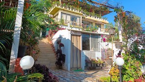 A two-story house with a balcony, surrounded by lush greenery and potted plants. - Strawberry County (Mahabaleshwar)