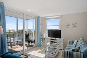 Un salon comprenant un canapé, une table basse, un téléviseur et un balcon avec une table et des chaises.