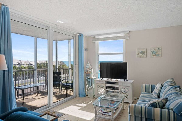 A living room with a sofa, a coffee table, a TV, and a balcony with a table and chairs.