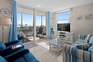Un salón con sofá, una mesa de centro de vidrio, televisor y balcón con vistas.