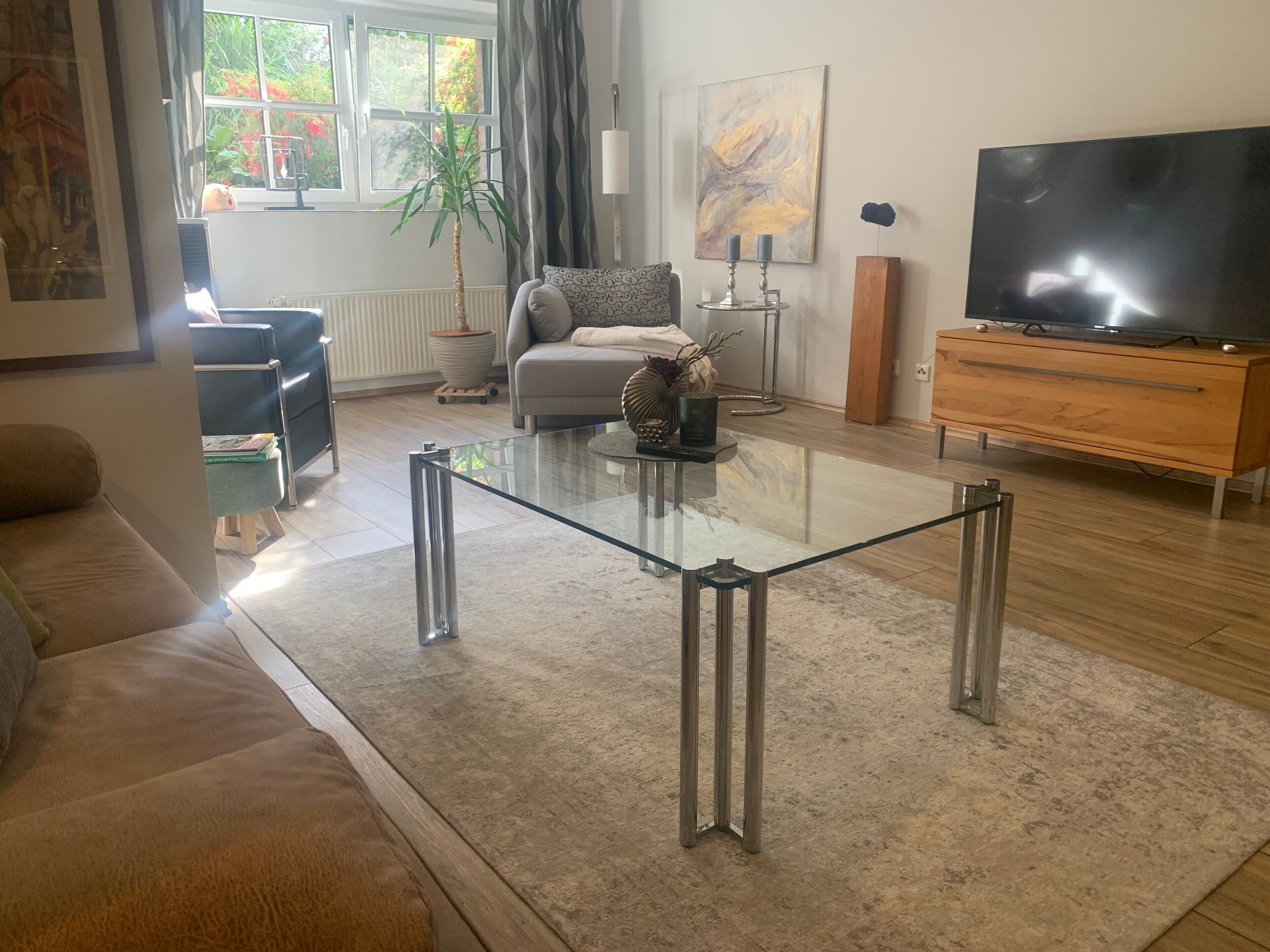 Un salon moderne avec une table basse en verre, un canapé, un téléviseur et une plante.