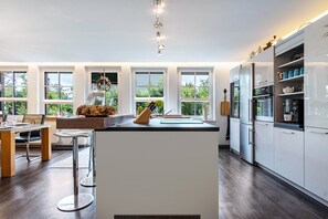 Une cuisine moderne avec des meubles blancs, un îlot central et un coin repas comprenant une table et des chaises en bois.