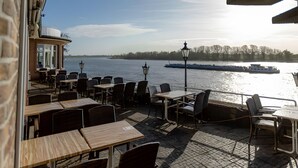Ein Außenbereich mit Tischen und Stühlen mit Blick auf einen Fluss und Boote.