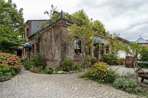 Ein Backsteinhaus mit Kopfsteinpflasterweg, umgeben von Grünpflanzen und einer hölzernen Bank.