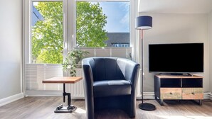 Ein modernes Wohnzimmer mit Ledersessel, TV-Schrank, Stehlampe und einem Fenster mit Jalousien.