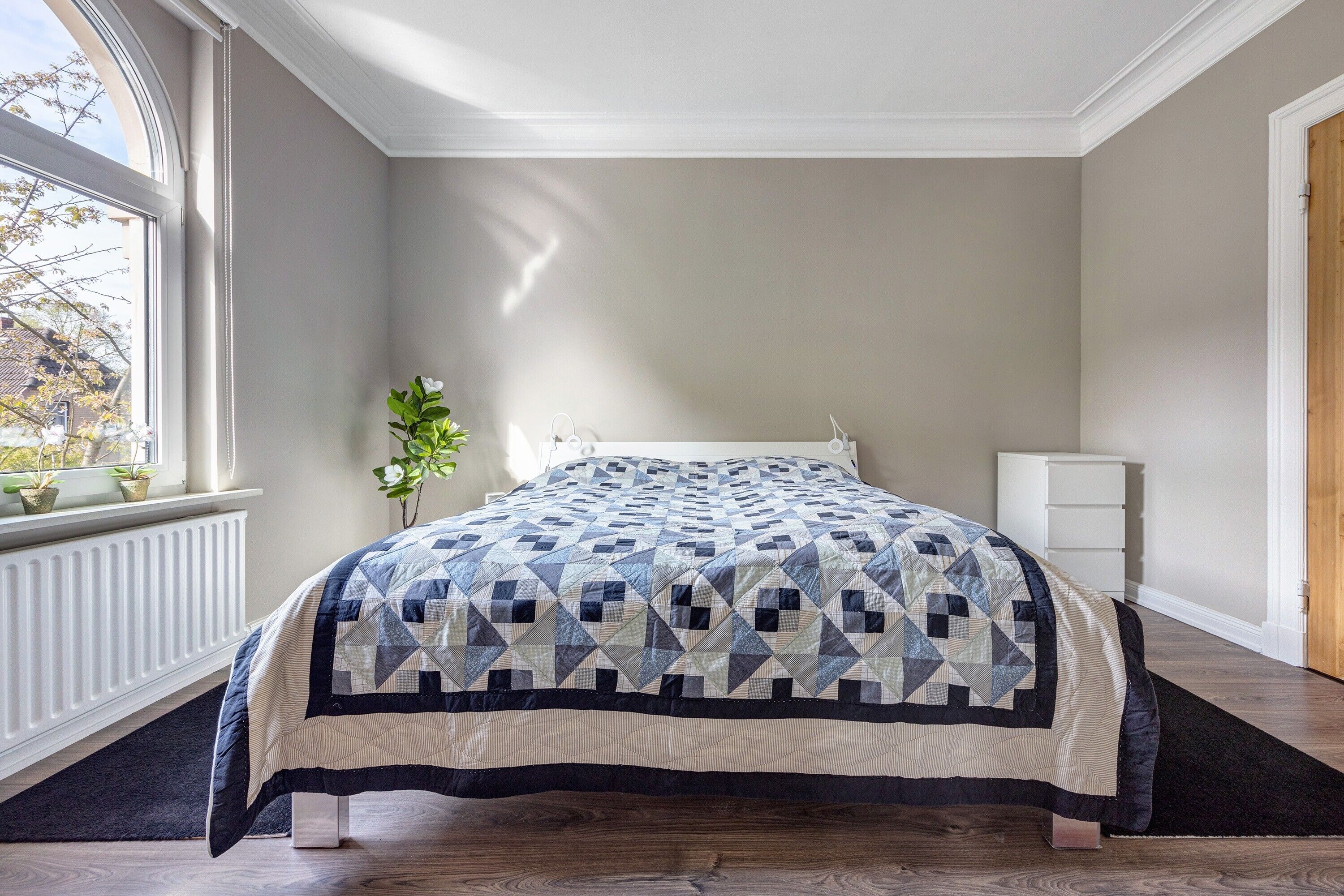 Een slaapkamer met een bed, een raam, een radiator en een nachtkastje.