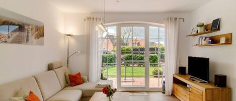 A living room with a sofa, coffee table, TV stand, and a view through a glass door.