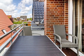 A balcony with a metal railing, a wicker chair, and a brick wall.