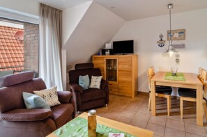A living room with a sofa, armchair, wooden cabinet, TV, dining table, and chairs.