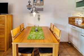 A wooden dining table with chairs, a green placemat, a glass, and a salt shaker.