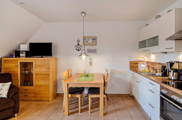 A modern kitchen with a dining table, chairs, a television, and a cabinet.