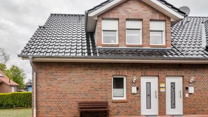A two-story brick house with a tiled roof, two white doors, and a small window.