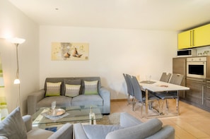 A living room with a grey sofa, a glass coffee table, and a dining area with a white table and chairs.