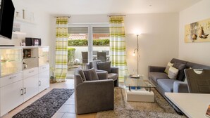 A living room with a sofa, armchair, TV, and a glass coffee table.