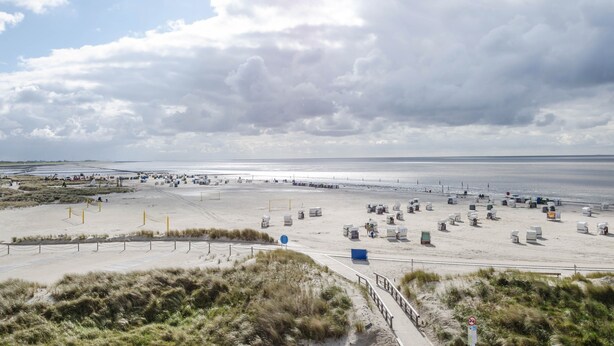 A beach with a sandy area, a few structures, and a body of water in the background.