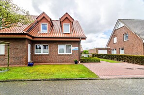 A two-story brick house with a tiled roof, a small front garden, and a paved driveway.
