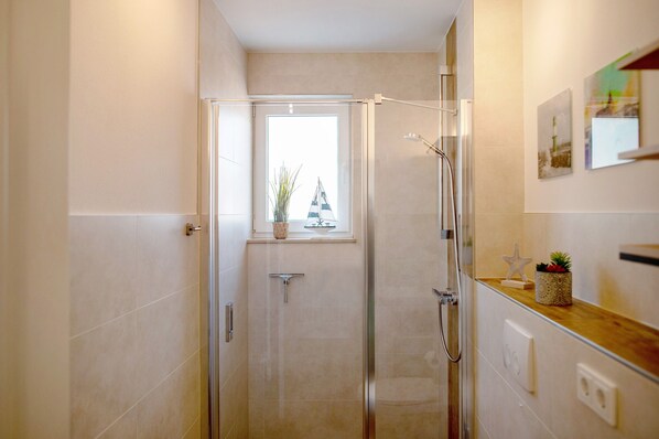 A modern bathroom with a glass shower enclosure, a small window with a plant, and a wooden countertop with decorative items.