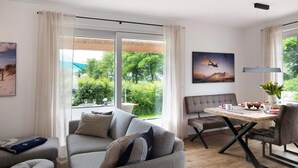 Un salon moderne comprenant un canapé, une table à manger avec des chaises, un banc et une grande fenêtre donnant sur un paysage verdoyant.