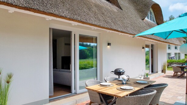 Une terrasse avec une table dressée pour le repas, des chaises en osier, un barbecue et un grand parasol.