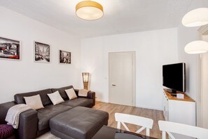 Un salon moderne avec un canapé, un téléviseur, une table à manger et des œuvres d’art accrochées au mur.