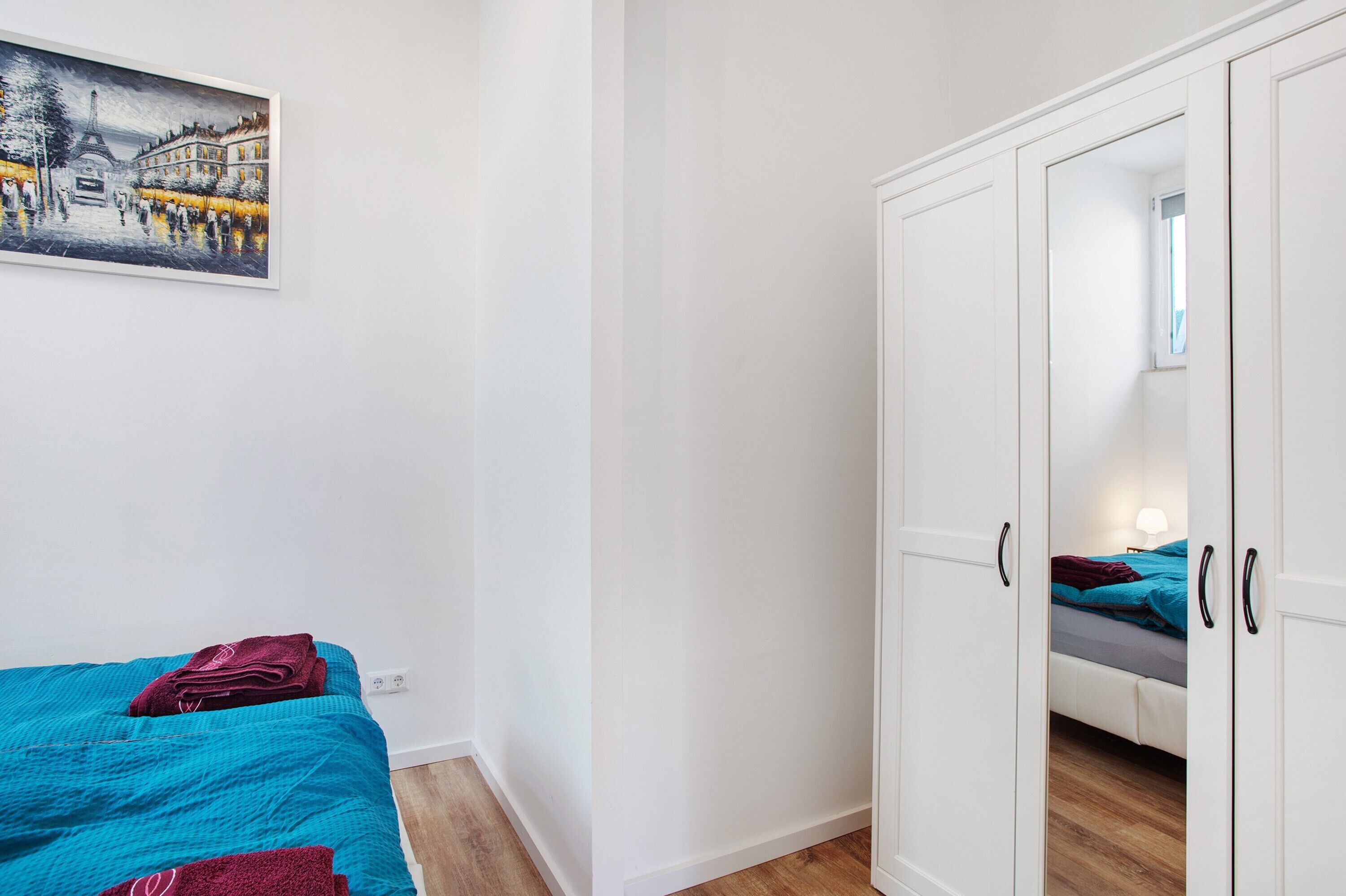 Ein Schlafzimmer mit Bett, Kleiderschrank, einem Bild an der Wand und einem Fenster.