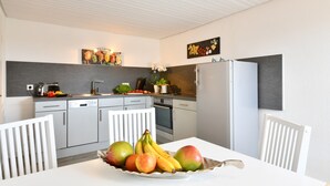 A modern kitchen with white cabinets, a dining table with a fruit bowl, and a refrigerator. - Holiday Apartment 'Dinkelbach Landhaus 1 A Charmant' with Lake View, Balcony and Wi-Fi (Bodolz)