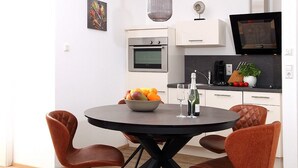 A modern kitchen with white cabinets, a built-in oven, a black countertop, and a dining area with a round table and brown chairs.