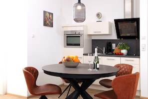 A modern kitchen with white cabinets, a built-in oven, a black countertop, and a dining area with a round table and brown chairs.