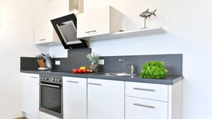 Una cocina moderna con armarios blancos, horno empotrado, un lavabo y una pequeña decoración con forma de pez en la pared.