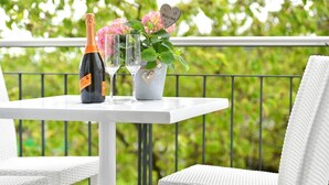 Una mesa blanca con una botella de champán, dos copas y un arreglo floral en un balcón.