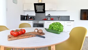 Una cocina moderna con armarios blancos, una estufa y una mesa de comedor con verduras frescas.