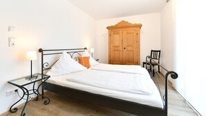 Un dormitorio con cama, mesitas de noche, un armario de madera y una silla.