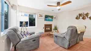 Ein Wohnzimmer mit zwei grauen Sofas, einem Deckenventilator, einem Kamin und einem großen Fenster.
