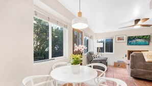 Ein helles Wohnzimmer mit einem weißen Tisch und Stühlen, einem grauen Sofa und einem Deckenventilator.