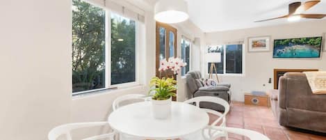 A bright living room with a white table and chairs, a gray sofa, and a ceiling fan.
