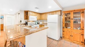Eine moderne Küche mit Granitarbeitsplatten, Holzschränken, einem weißen Kühlschrank und einem eingebauten Backofen.
