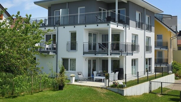 A multi-story residential building with balconies, a patio area, and a well-maintained lawn.
