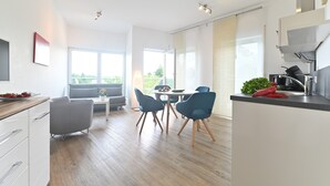 A modern kitchen with a dining area, large windows, and a view of greenery.