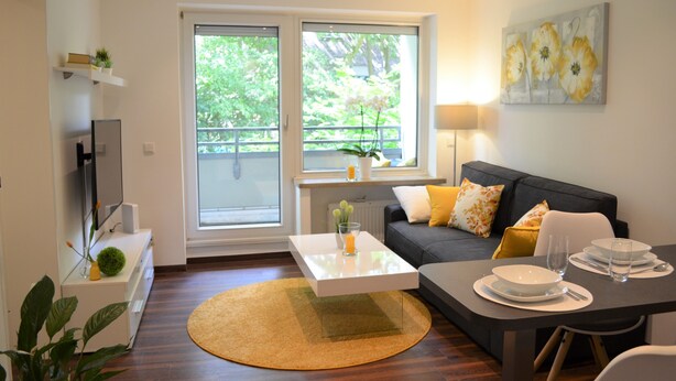 A modern living room with a sofa, coffee table, dining table, and a large window with a view of greenery.