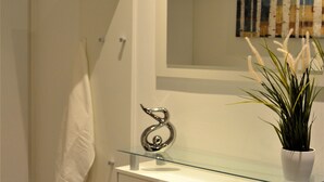 A bathroom with a glass sink, a white towel hanging, a potted plant, and a mirror above the sink.