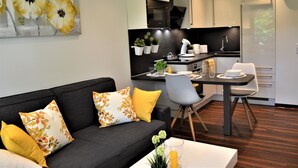 A modern kitchen with white cabinets, a dining area with a table and chairs, and a living room with a sofa and decorative pillows.