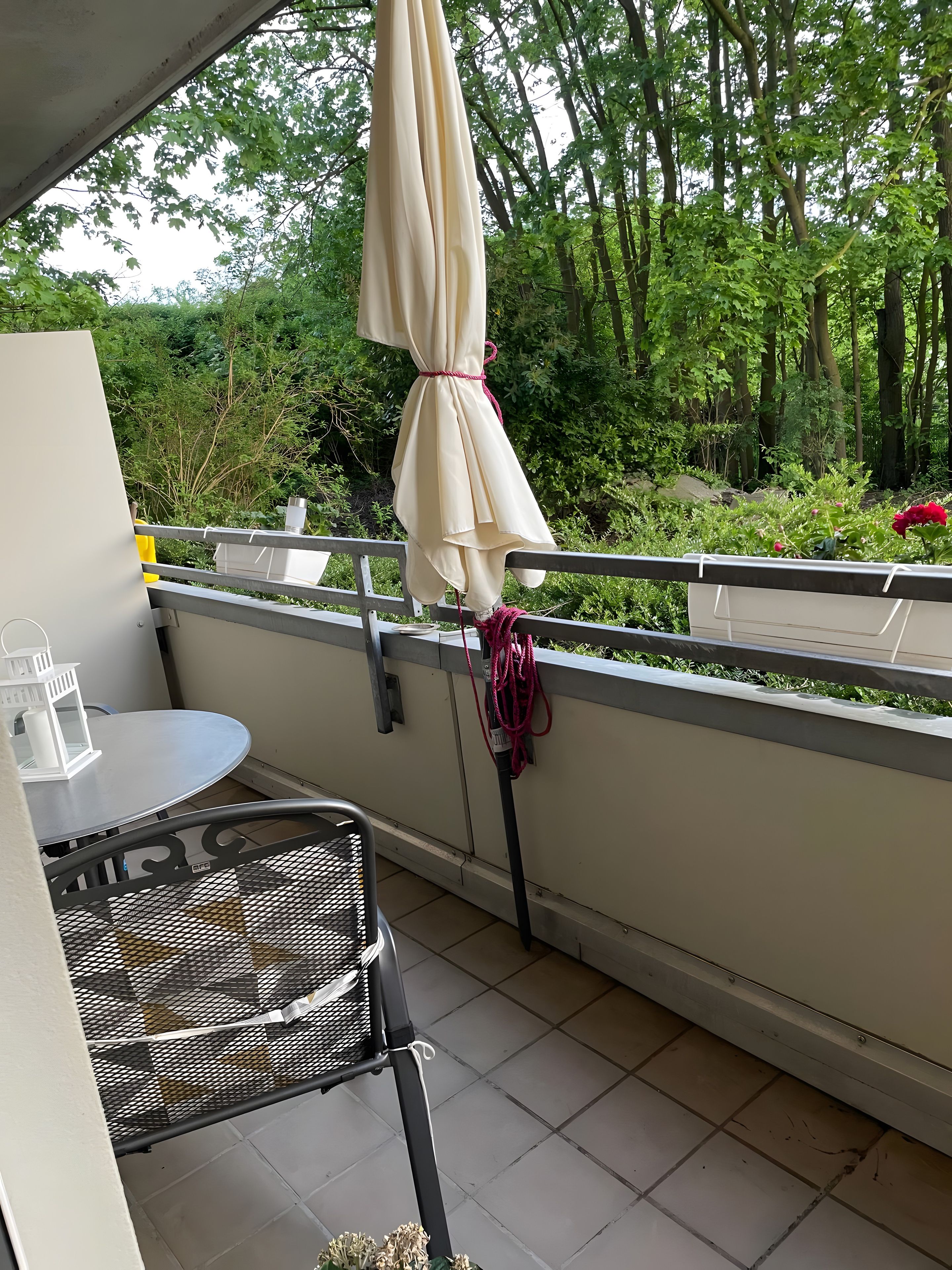 En balkon med et bord og stole, en markise samt udsigt til grøn vegetation.
