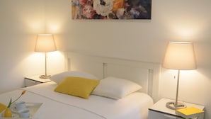 A hotel room with a bed, two bedside lamps, a nightstand, a tray with a cup and a book, and a painting on the wall.