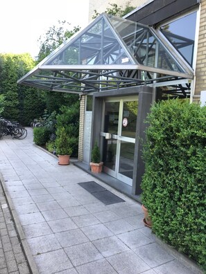 A building with a glass entrance, potted plants, and a metal structure above the door.