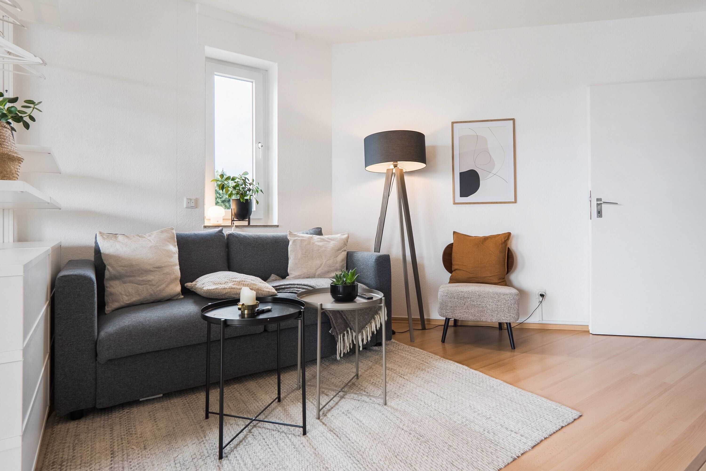 Een moderne woonkamer met een grijze bank, een klein rond tafeltje, een vloerlamp en een stoel.